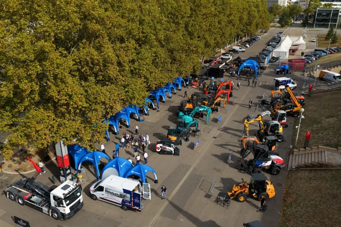 Vue aérienne de la manifestation We Love Machines organisée par Chrono Flex à Lyon, avec des engins de chantier exposés, des stands de partenaires et des visiteurs circulant dans les allées.